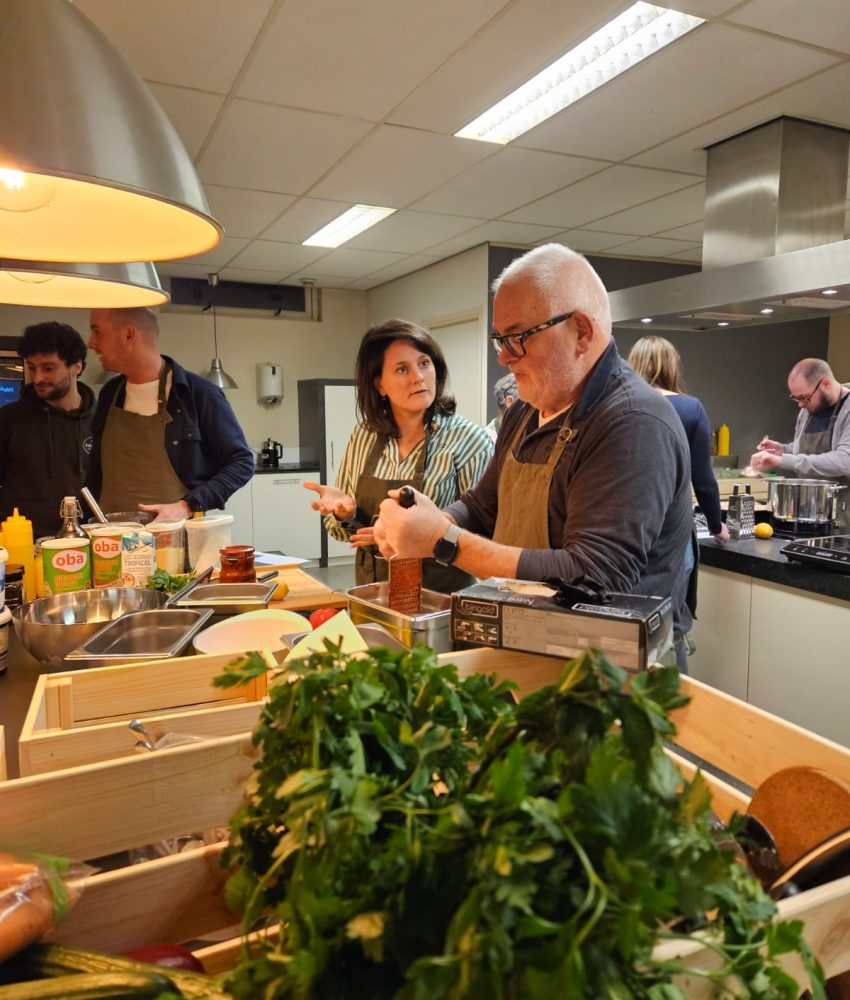 Samen koken: Collega's werken in duo's om groenten te snijden en gerechten te bereiden, met een ontspannen en vrolijke sfeer.