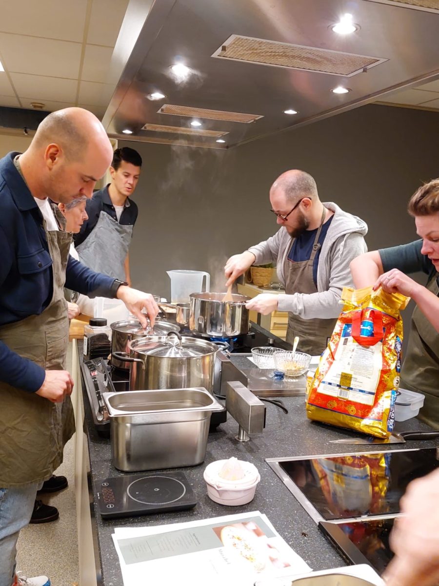 bedrijfsuitje samen koken: Collega's werken in duo's om groenten te snijden en gerechten te bereiden, met een ontspannen en vrolijke sfeer.